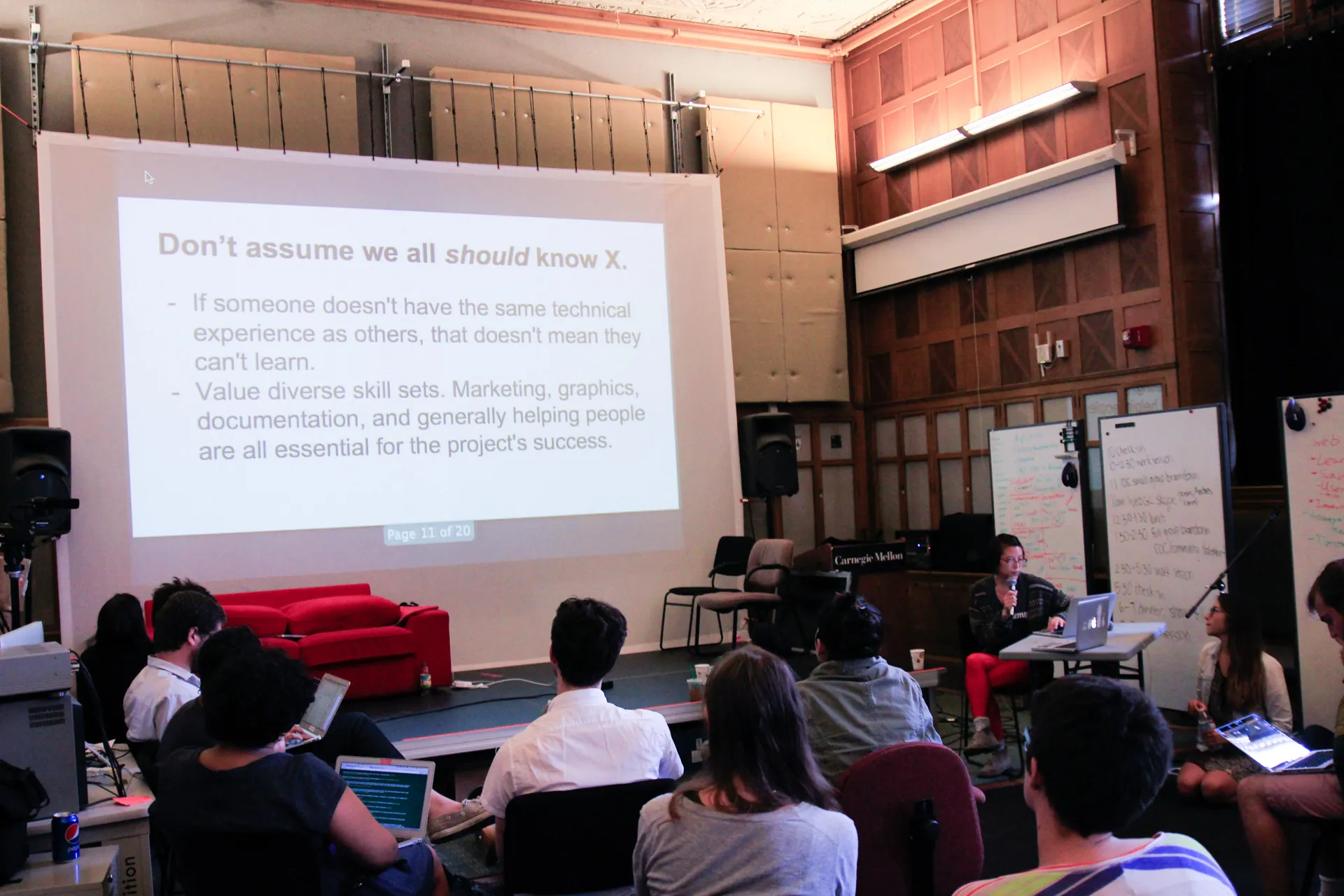 Woman speaking into a microphone about valuing different skill sets while a group of participants with laptops look at her powerpoint in a classroom