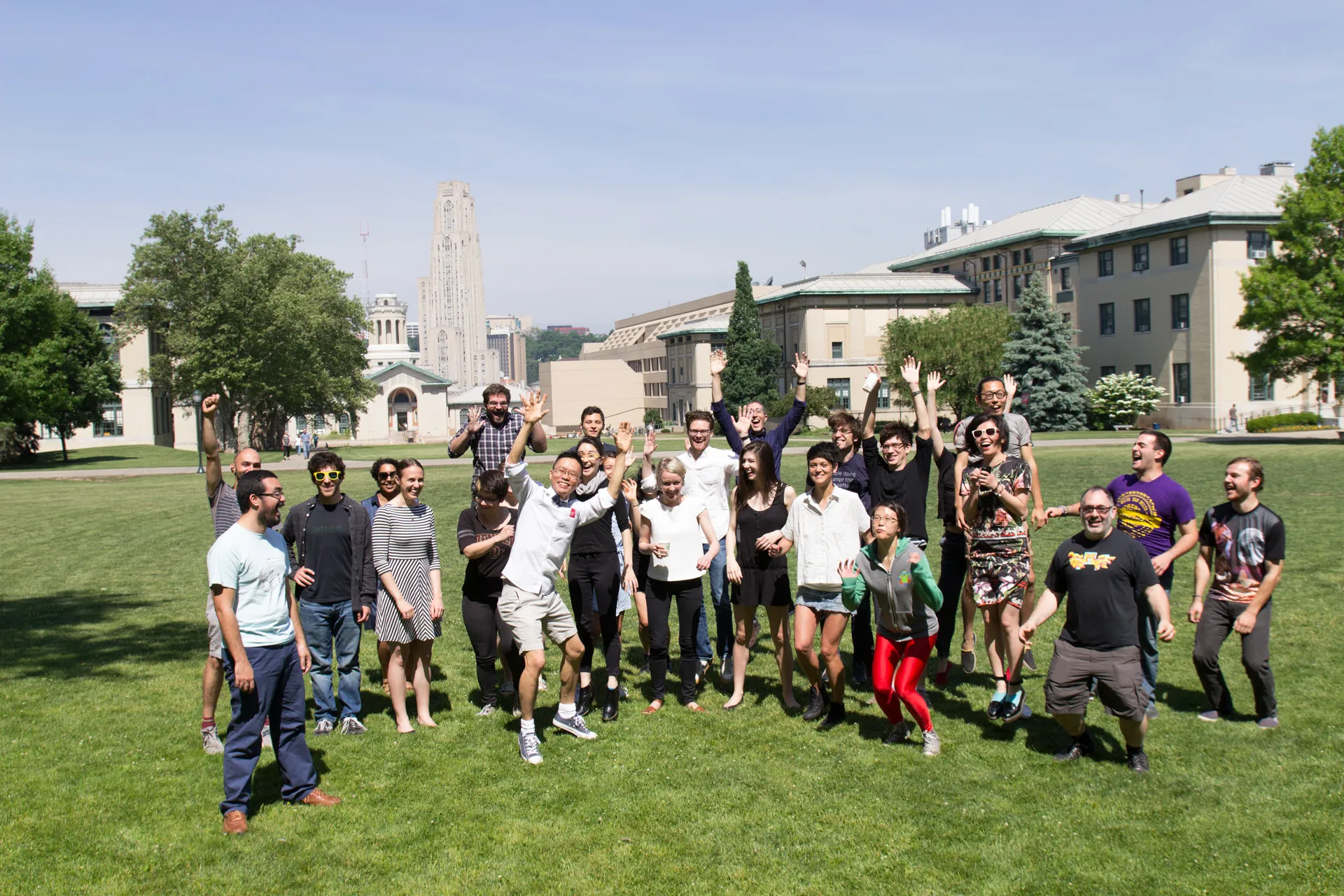 Participants jump, smile and throw their hands in the air on a green lawn