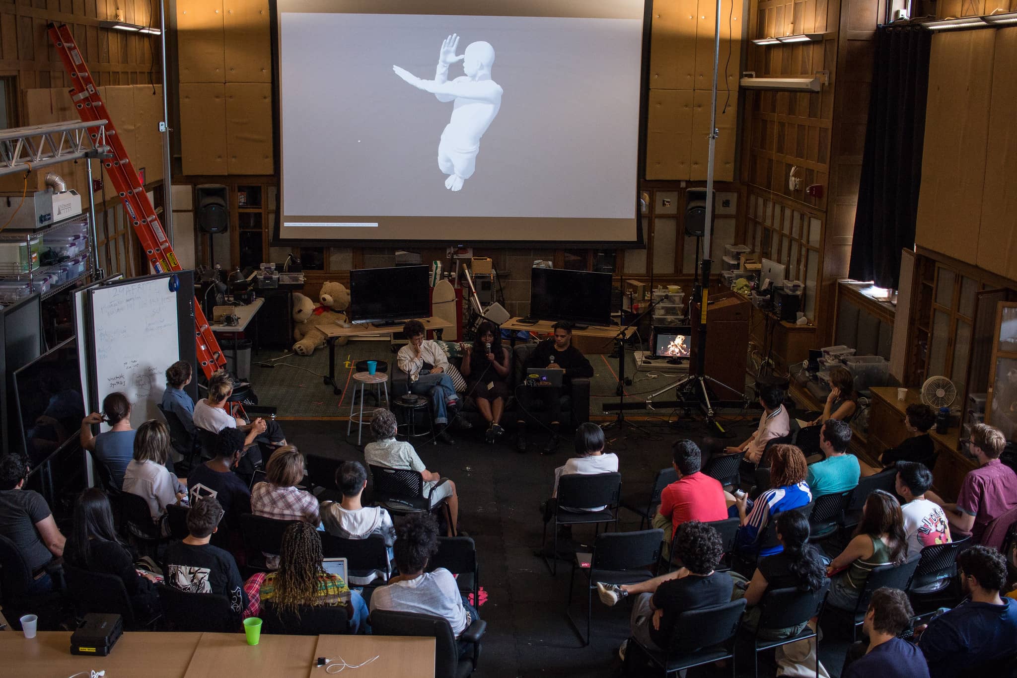 Overhead view of participants listening to a panel of people with an image of a 3d rendered man on it