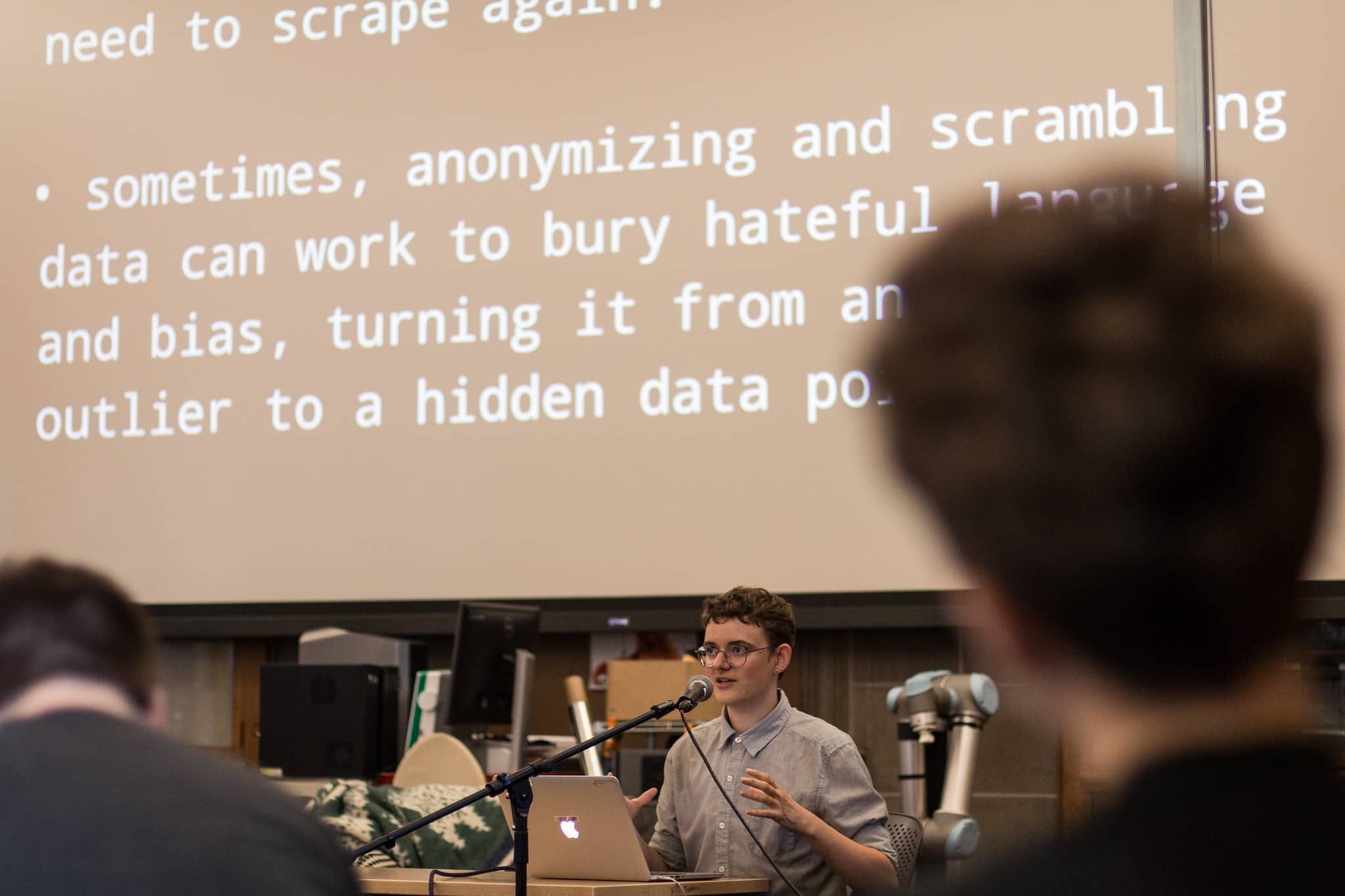 Participant speaks at a podium in front of projected text about the problem with anonymyzing data