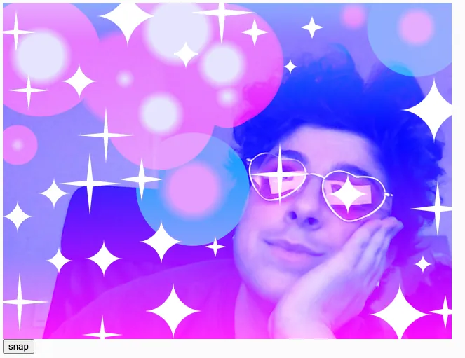 A white person with short, dark curly hair wears pink heart-shaped glasses and a dark sleeveless shirt. He places his hand on his cheek and looks diagonally to the left, smiling softly. A vertical linear blue to pink gradient is overlaid. On top of that, we see a mixture of angular and curved white 4-pointed sparkles of varying sizes, with an angular sparkle over the left lens of his glasses, and a curved sparkle over the right lens. We see pink and blue radial gradient circles layered on top, creating a lens flare effect.