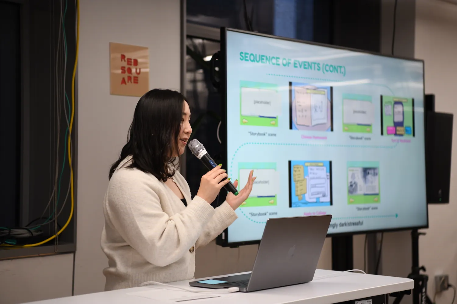 Jackie Liu holding a mic next to a big t.v. screen that has a series of screenshots of their game project “Chao bing”.