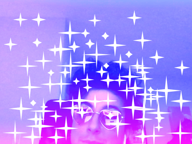 短い暗いカールヘアとピンクのハート型メガネを着けた白人が頭を傾けています。写真全体に様々なサイズの4点の角張った白い輝きを追加しました。また、その人のハート型メガネの各レンズの上にも輝きが配置されています。